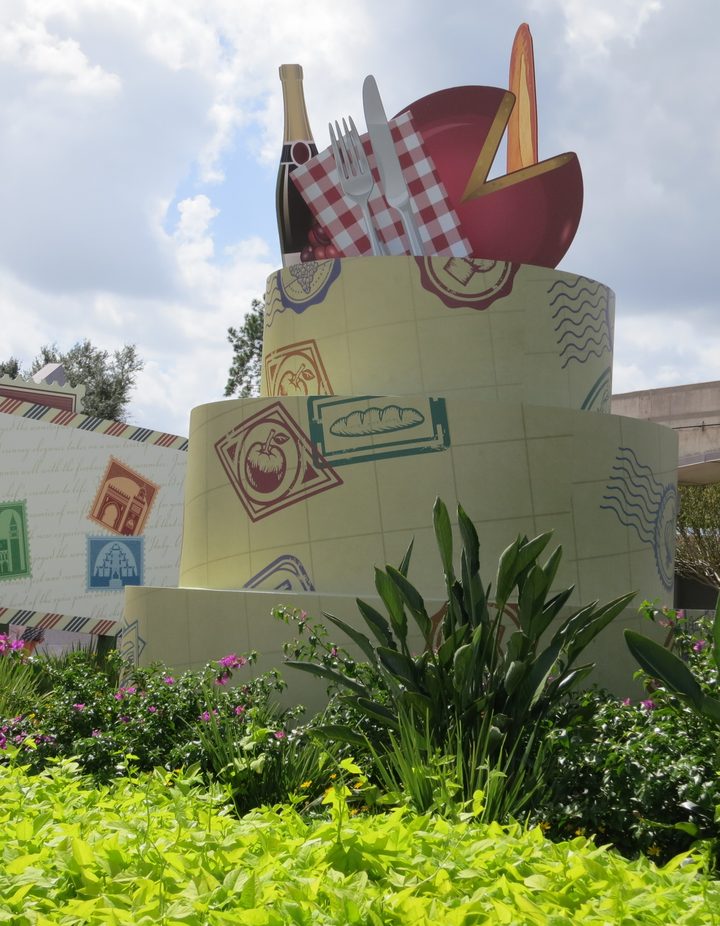 Postcard-stack festival sculpture topped with champagne, cheese, and a picnic napkin